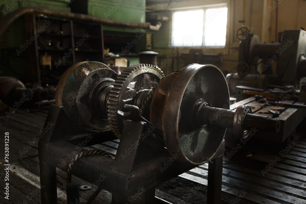 Vintage machinery in old factory, industrial gears on workbench. Historic manufacturing equipment, workshop tools.
