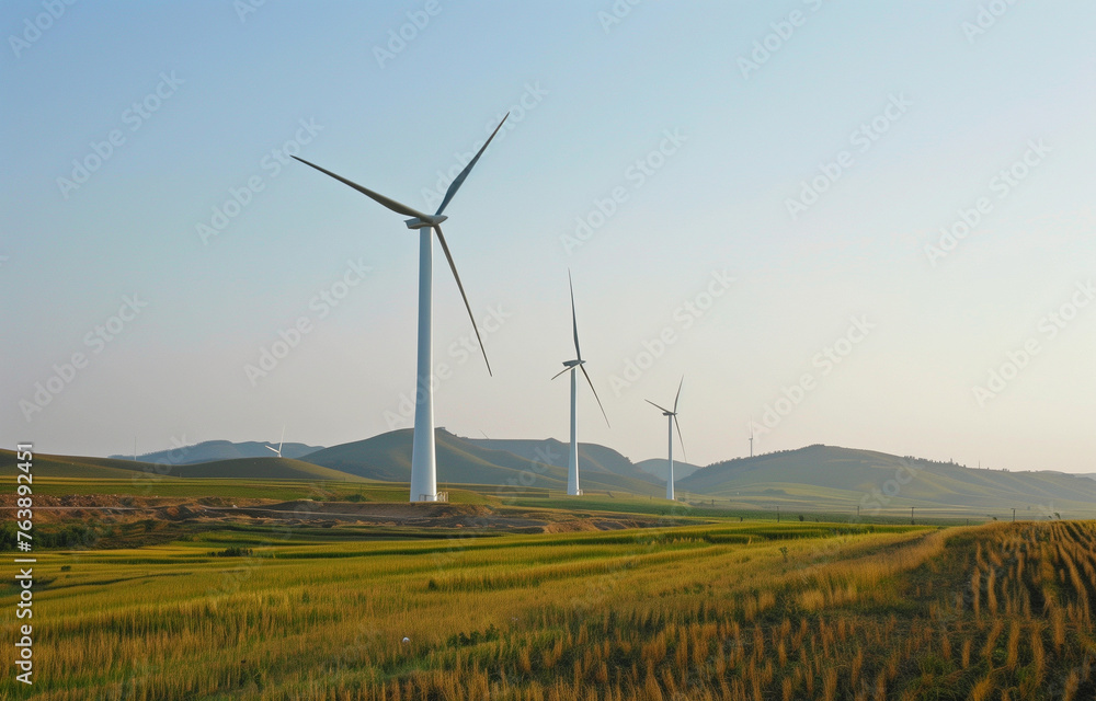 Obraz premium Wind turbines stand tall in a grassy field, framed by mountains