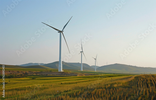 Wind turbines stand tall in a grassy field, framed by mountains