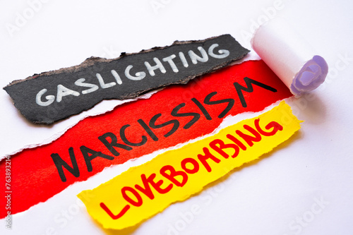 Word Narcissism on red surface, under torn white sheets. Alongside, cards with the words gaslighting and lovebombing.
