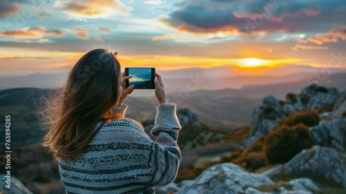 woman traveler enjoying outdoor adventure capturing sunset sky and scenic mountains in casual sweater photo