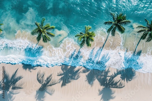 Aerial view of Aqua marine ocean with waves breaking on white sand beach with palm tree shadows