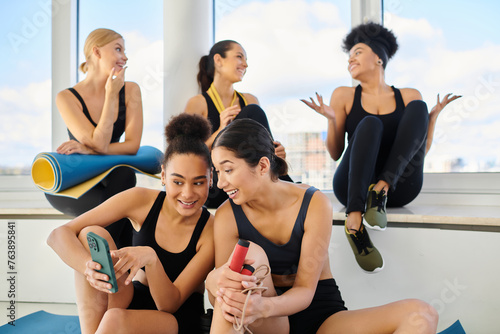 group of cheerful five female friends in sportswear chatting after workout in pilates studio