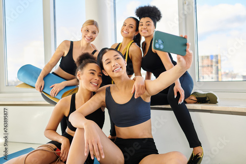 five cheerful interracial female friends in sportswear taking selfie after pilates workout, women