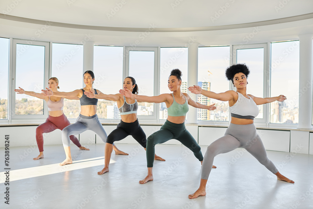 group of young diverse women in sportswear practicing pilates with female african american trainer