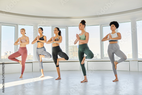 group of young five diverse women in sportswear practicing yoga exercise together in studio