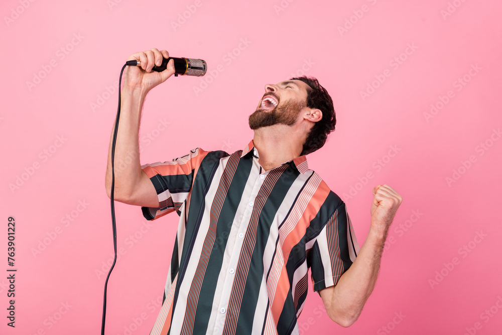 Photo of young funny man showman rock roll singer holding microphone raised fist up talented artist isolated on pink color background - obrazy, fototapety, plakaty 