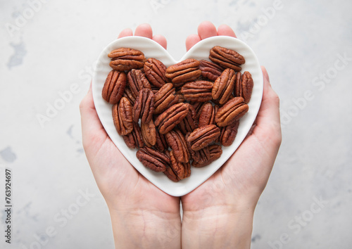 Female hands holding heart shaped plate with peeled pecan nuts on light background.Macro.