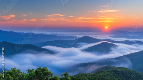 Misty mountain landscape with clouds, fog, and orange sunrise sky creating a serene morning view