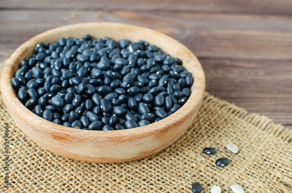 Raw black bens in a wooden bowl on burlap on a wooden table. Rural style. Vegetarian food concept. Horizontal orientation. Selective focus. Raw black bens in a wooden bowl on burlap on a wooden table. Rural style. Vegetarian food concept. Horizontal orientation. Selective focus.