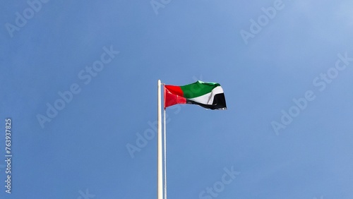 UAE country national flag hanging and flying crinkled high on a flagpole with a blue sky background. The United Arab Emirates Flag Day celebration concept. Flag wave during wind spectacular view.