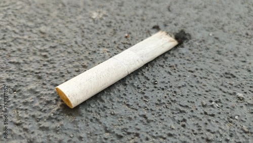 A white cigarette butt was thrown away and isolated on the ground pavement floor. Selective focus macro extreme closeup of burnt or consumed cigarette filter end. Unhealthy tobacco addiction concept.