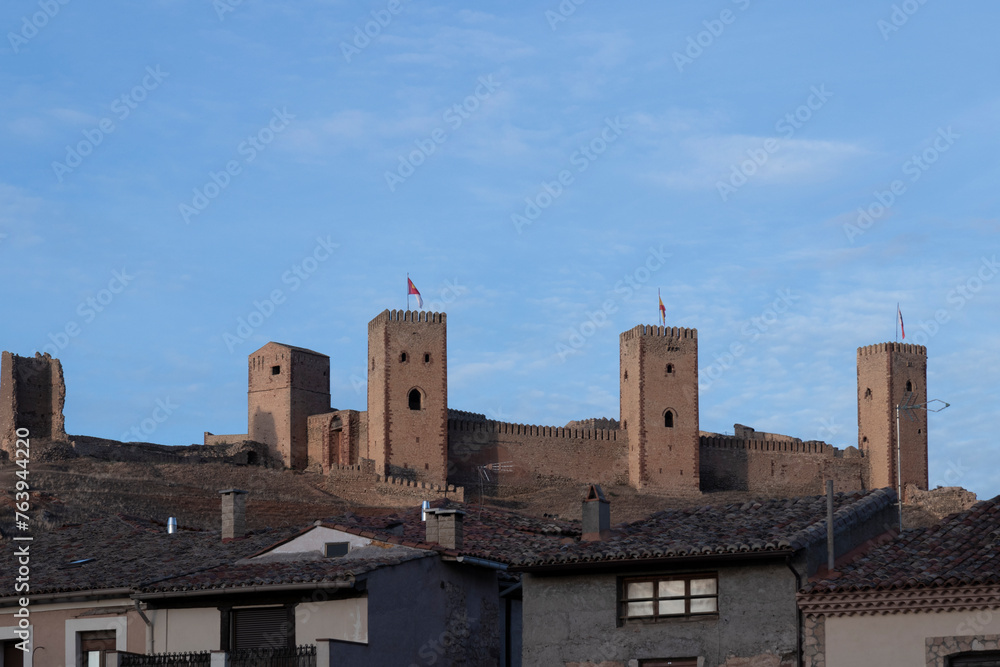 An ancient castle with tall towers overlooks a modern town, showcasing architectural contrast and historical preservation