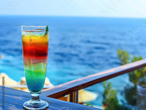 tall glass with a three-color drink on the balcony table on a blurred sea background.