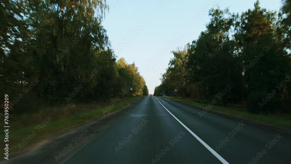 View through rear windshield windscreen of car in motion, back glass screen. Single carriageway with two-lane road along forest. Countryside roadway out of town. Travel journey trip in autumn fall View through rear windshield windscreen of car in motion, back glass screen. Single carriageway with two-lane road along forest. Countryside roadway out of town. Travel journey trip in autumn fall