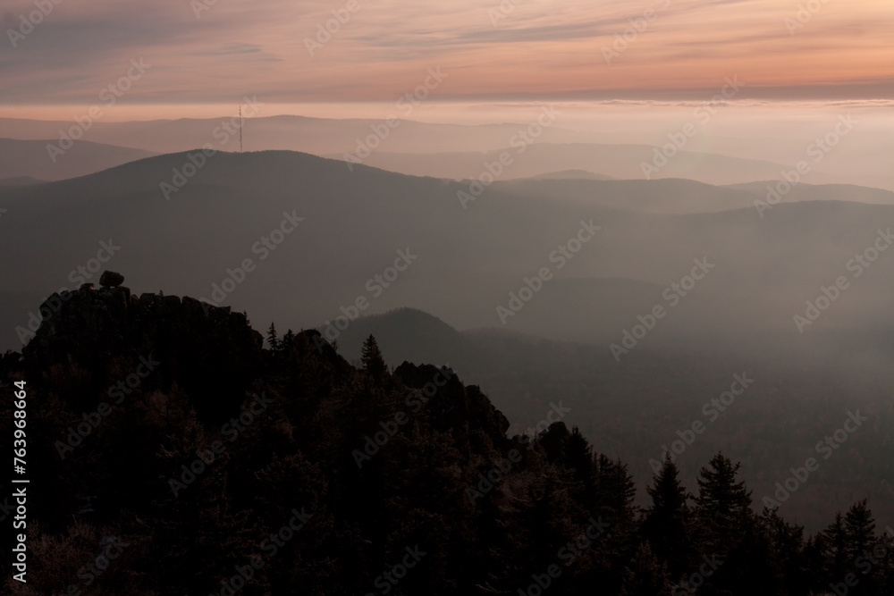 Sunset over foggy highland mountain range with trees in foreground