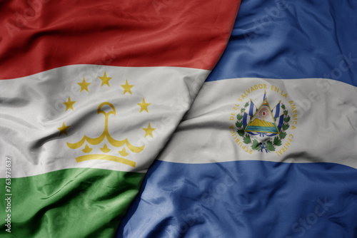 big waving national colorful flag of el salvador and national flag of tajikistan.