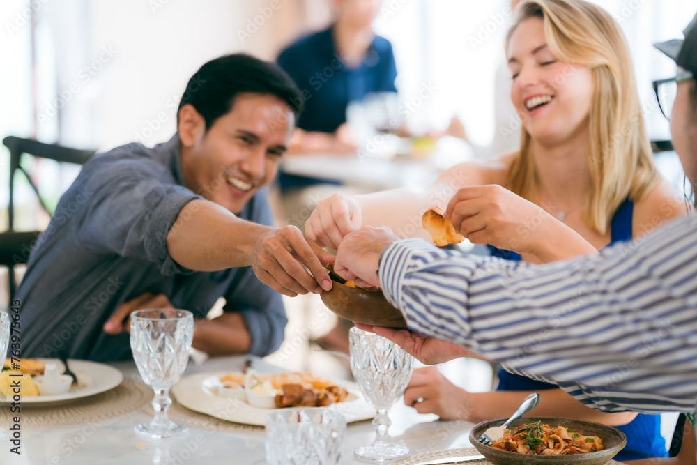 Happy young people laughing enjoying meal having fun sitting together at restaurant table, diverse friends person share lunch at meeting, talking and chatting together in holiday lifestyle