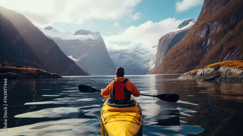 A tourist on a yellow kayak floats on a lake near the snowy mountains.