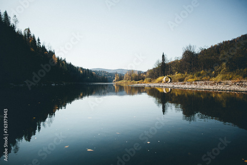 A serene lake with trees on the shore, framed by mountains and a cloudy sky