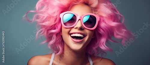 A woman with pink hair and sunglasses smiling and wearing sunglasses.