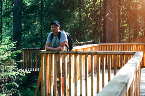 A young man walks through the park. A man with a backpack on his shoulders stands thoughtfully looking at the forest. Spending time outdoors. Front view