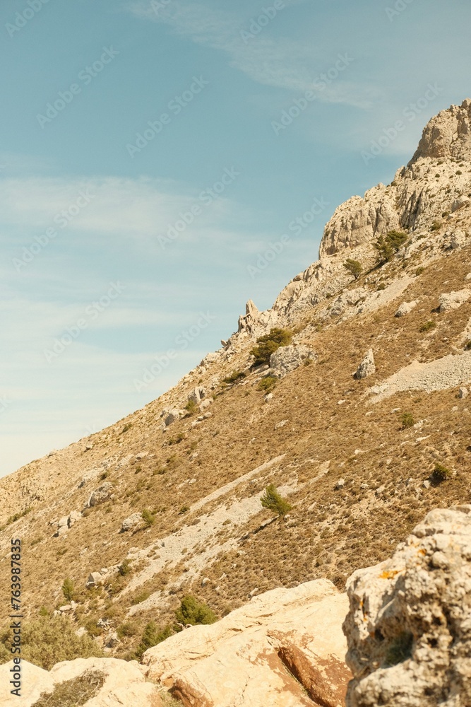 Film style photography of an earth tone landscape in abstract composition. It features a mediterranean mountain, Serra de Bernia, close to alicante, with blue sky.
