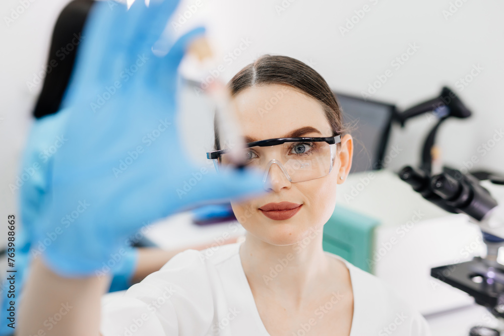 A female laboratory assistant conducts an experiment in a scientific laboratory, studying a blood sample with a virus. Concept for Covid treatment, scientific experiments and medical research. A female laboratory assistant conducts an experiment in a scientific laboratory, studying a blood sample with a virus. Concept for Covid treatment, scientific experiments and medical research.