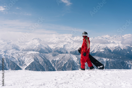 Snowboarder woman standing with snowboard in beautiful mountain peaks covered with snow on background