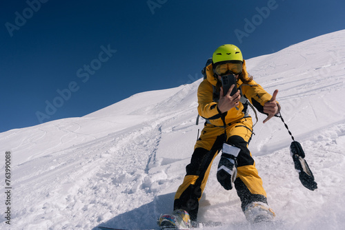 Woman snowboarder riding and taking photo on mobile phone on slope of powdery snow in high mountains. Freeride at ski resort