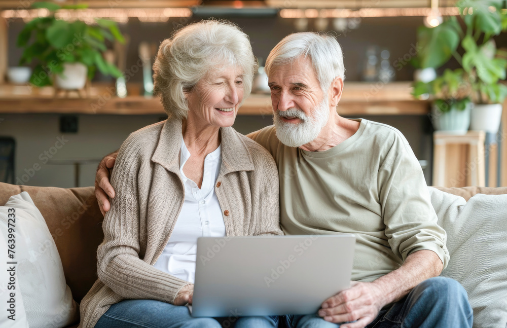 Happy mature senior couple using laptop sit on sofa at home. Smiling senior old adult man and woman using laptop to shop online. Retirement and happy senior lifestyle concept. 