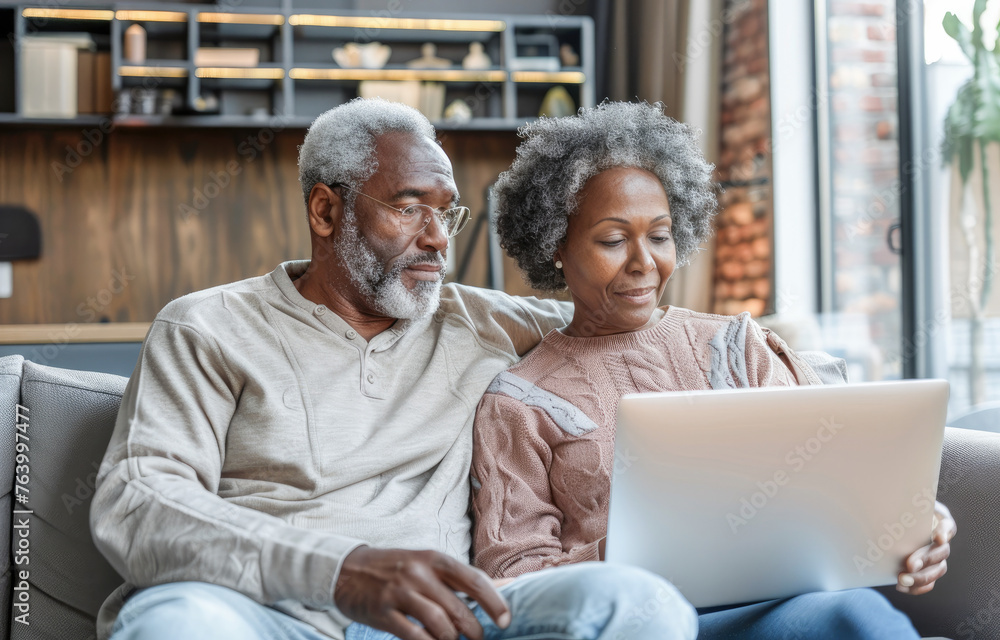 Happy mature senior couple using laptop sit on sofa at home. Smiling senior old adult man and woman using laptop to shop online. Retirement and happy senior lifestyle concept. Happy mature senior couple using laptop sit on sofa at home. Smiling senior old adult man and woman using laptop to shop online. Retirement and happy senior lifestyle concept.