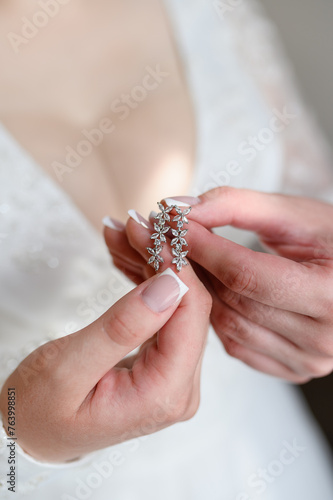 Beautiful earrings in hands of bride, close-up. Concept of bride's morning, preparation for wedding ceremony, wedding day. Stylish wedding accessory for the bride. Vertical.