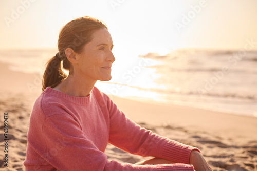 Retired Senior Woman On Vacation Sitting On Beach Shoreline Watching Sunrise