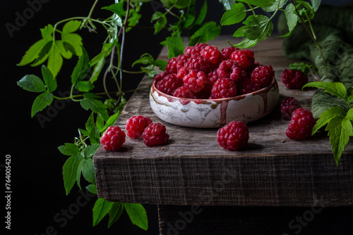 Still life with raspberries and curly green branches on an old wooden table