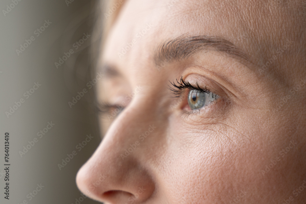 Obraz premium A close-up depicts part of a womans face, highlighting her eye, eyelashes, and the texture of her skin. Her gaze seems reflective and introspective, capturing a moment of thought or observation