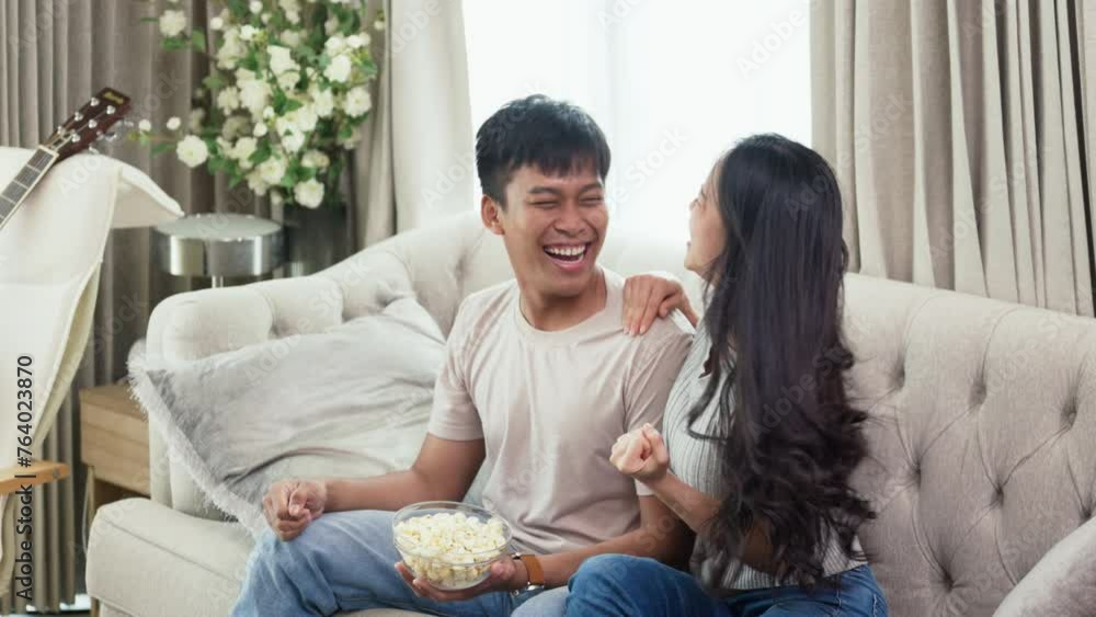 Overjoyed Asian couple sitting on couch and watching sports game together Overjoyed Asian couple sitting on couch and watching sports game together