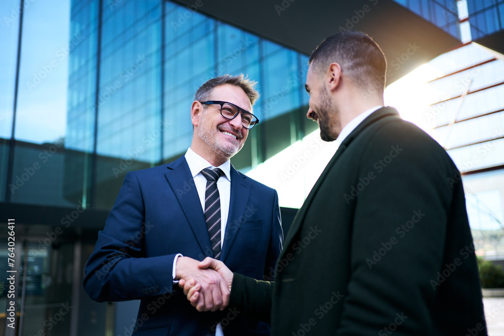 Cheerful smiling team of diverse business man in formal suit shaking hands with positive faces gathered outside the work building. Happy corporate work team closing a deal in a corporate area Cheerful smiling team of diverse business man in formal suit shaking hands with positive faces gathered outside the work building. Happy corporate work team closing a deal in a corporate area