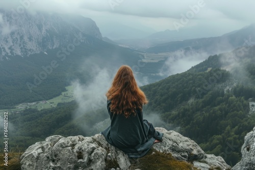 A woman is meditating on the edge of a cliff with a very beautiful view of the mountains at sunset. Woman sitting on the edge of a mountain. © Zero Zero One