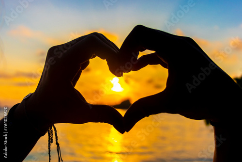 Heart made of hands with turquoise water and sunset Maldives.