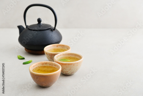 Black cast iron teapot and three ceramic cups of green tea