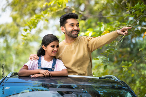 Happy indian father showing nature to daughter on car sunroof - concept of vacation, traveling and relationship