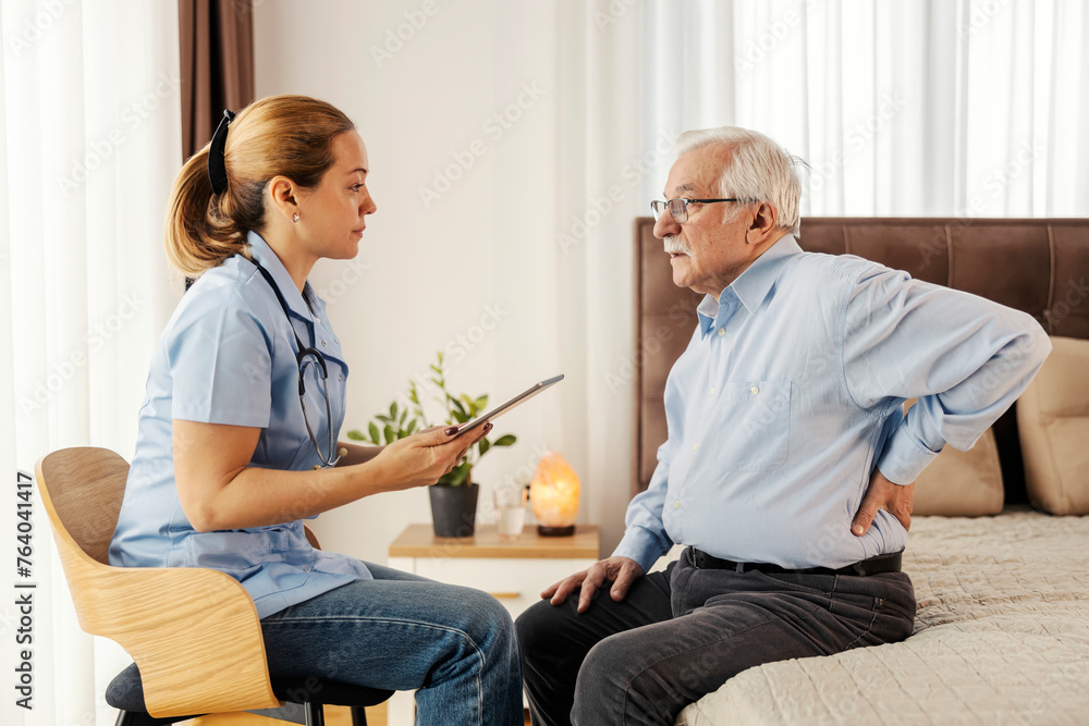 Obraz premium A senior man with back pain is sitting on a bed during doctor's visit at home.