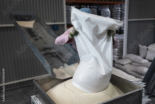 A worker at a manufacturing plant pours a bag of sugar onto a conveyor belt for further processing