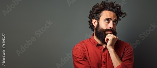 A bearded man wearing a red shirt is looking up in contemplation