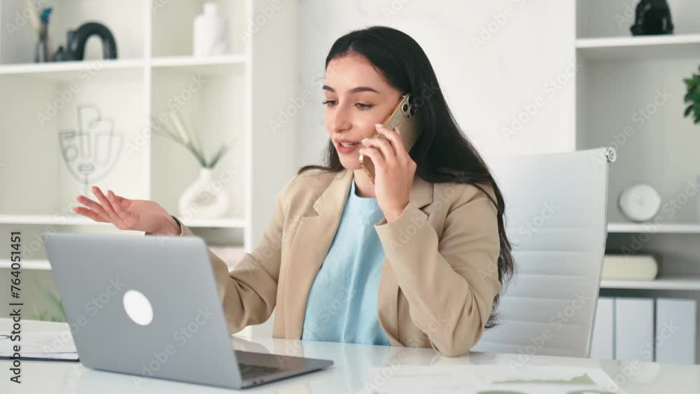 Busy successful pretty indian or arabian business woman, company employee, ceo, sits in the modern office, talking by smartphone, having conversation with partner or client, using laptop, smile Busy successful pretty indian or arabian business woman, company employee, ceo, sits in the modern office, talking by smartphone, having conversation with partner or client, using laptop, smile