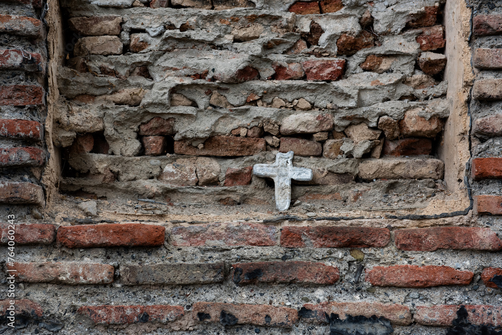A small, white cross embedded in a crumbling brick wall in Tbilisi, Georgia. A small, white cross embedded in a crumbling brick wall in Tbilisi, Georgia.