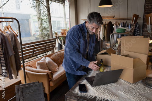 Hispanic male using a laptop to pack online customer orders in his store