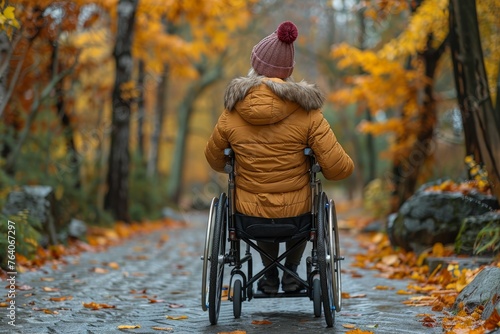 Rear view of a woman in a wheelchair navigating an autumnal path strewn with fallen leaves, symbolizing accessibility and independence