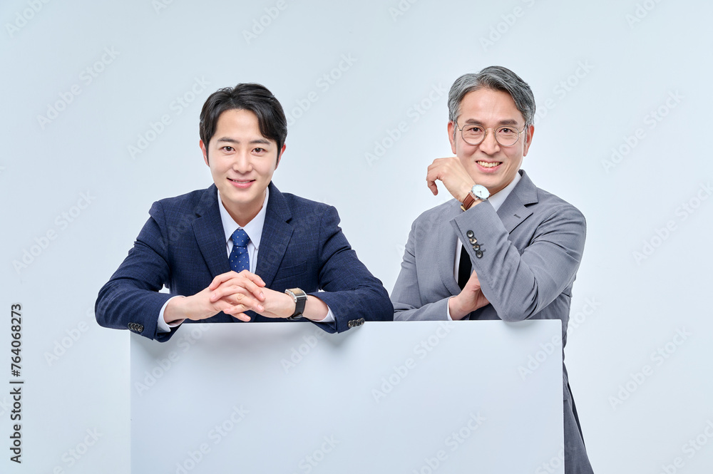 A young office worker man wearing a suit and glasses and a middle-aged man are holding a white board together and posing with various confident expressions and poses. A young office worker man wearing a suit and glasses and a middle-aged man are holding a white board together and posing with various confident expressions and poses.
